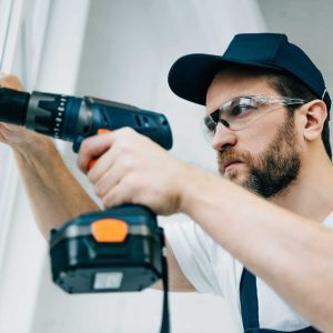 adult-repairman-in-goggles-fixing-window-handle-by-electric-drill-e1663969255653-qbc434mhj50w15htbympitrdjwq4zit712csflo1iw
